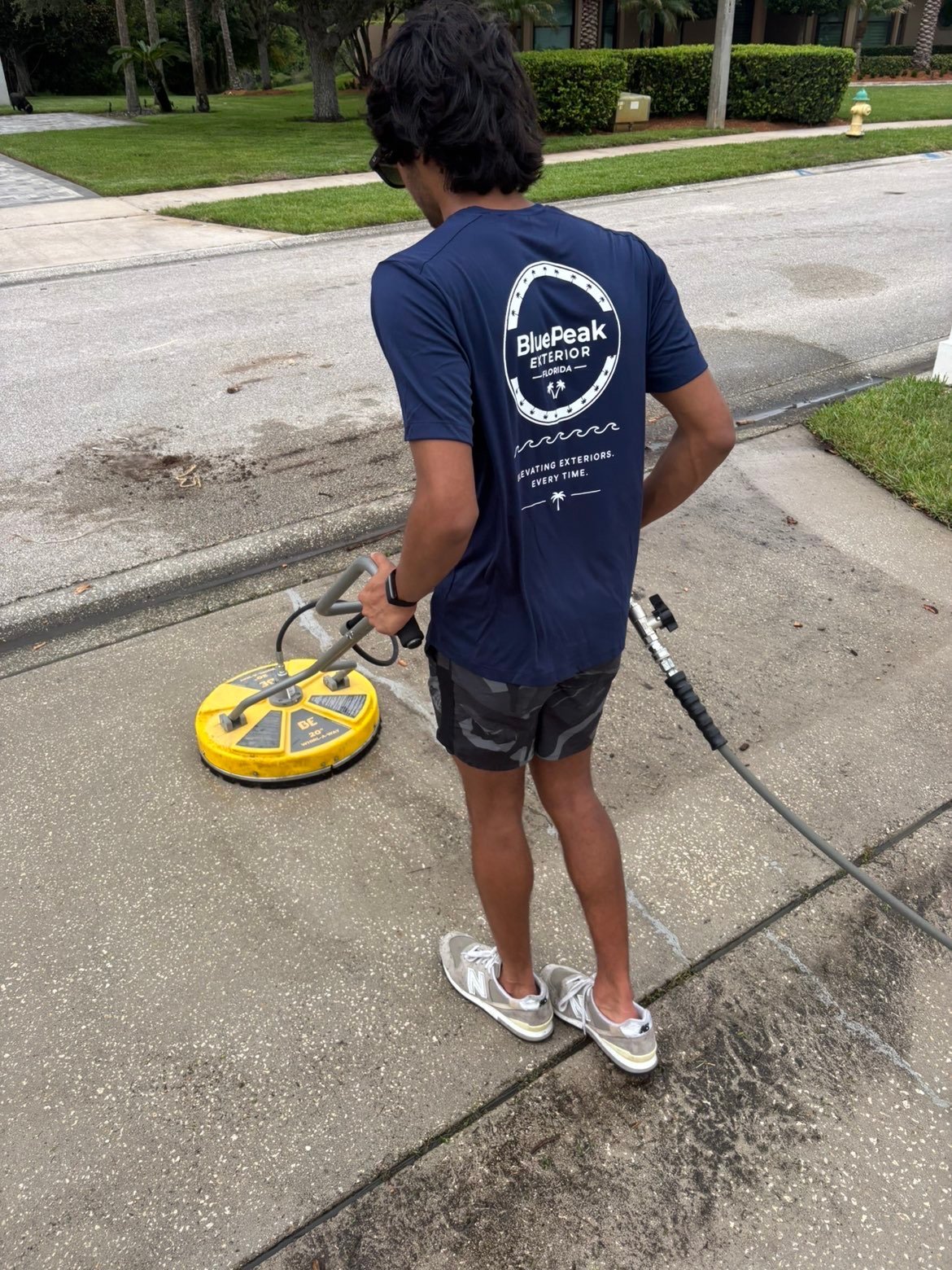 Person in BluePeak Expeditions shirt holding a yellow flying disc on a residential street